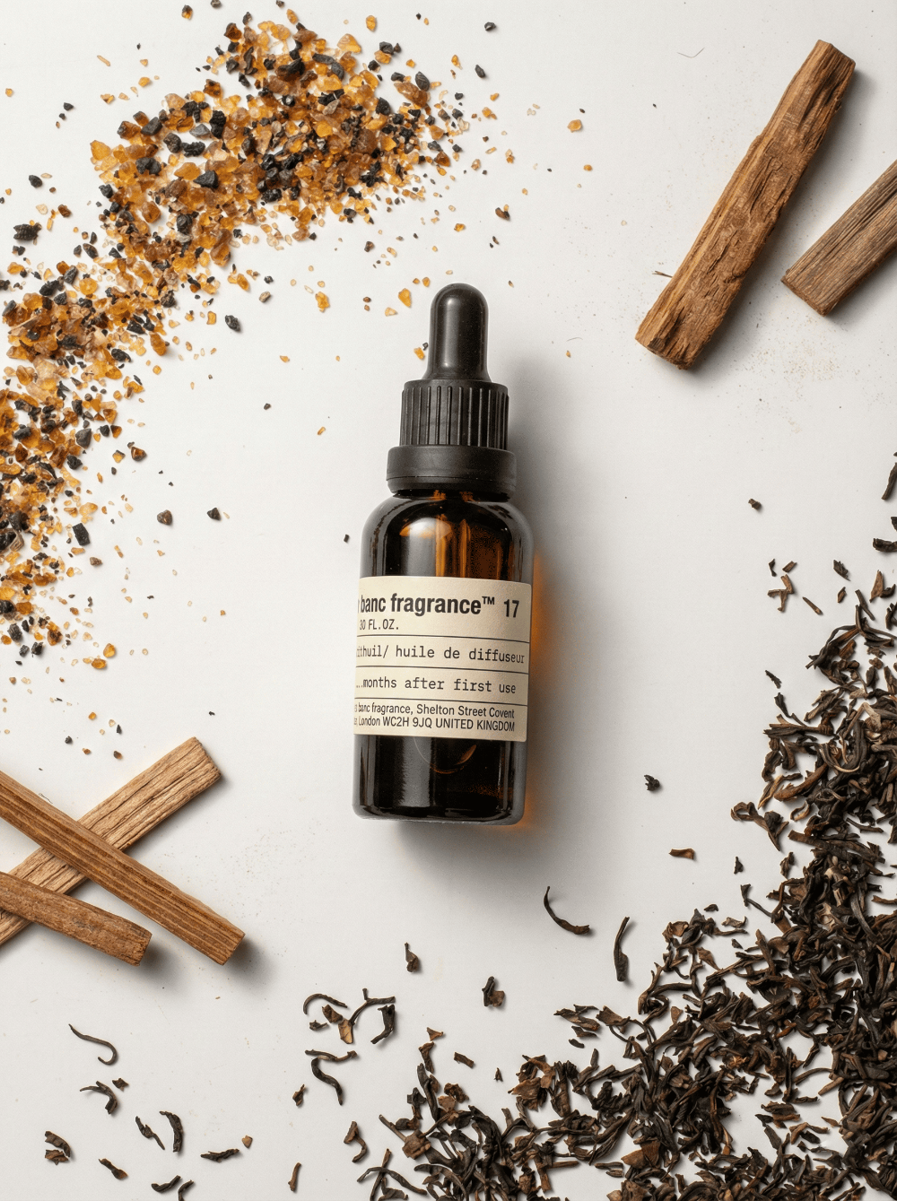 Charabanc Fragrance NO.17 Winds of Darjeeling essential oil bottle surrounded by loose black tea leaves, guaiac wood sticks, and amber resin grains.