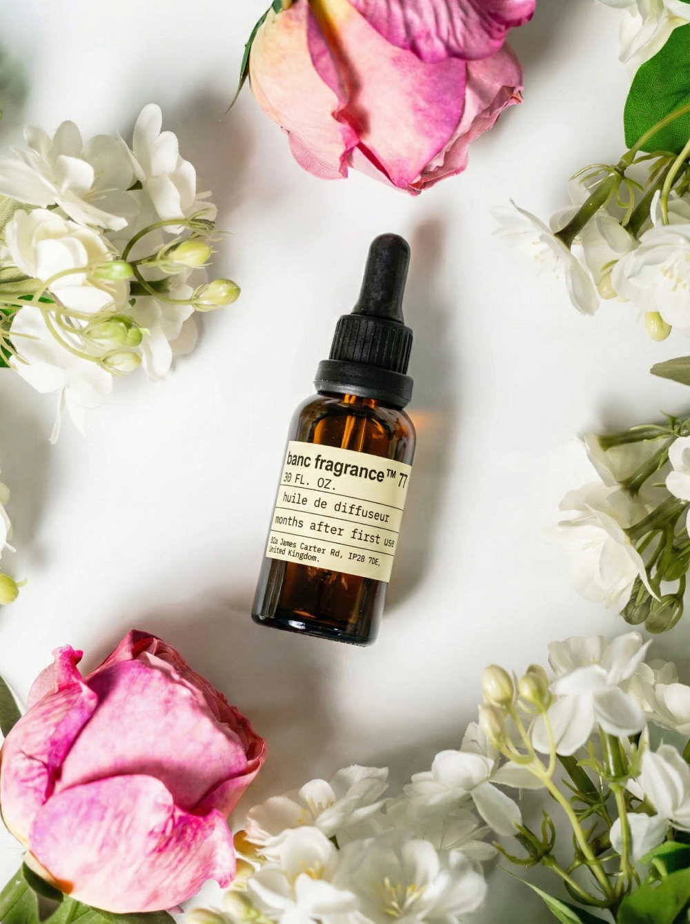 Charabanc Fragrance NO.71 Blossom Muse essential oil bottle centered among elegant pink roses and white orange blossoms, representing a radiant citrus-floral scent.