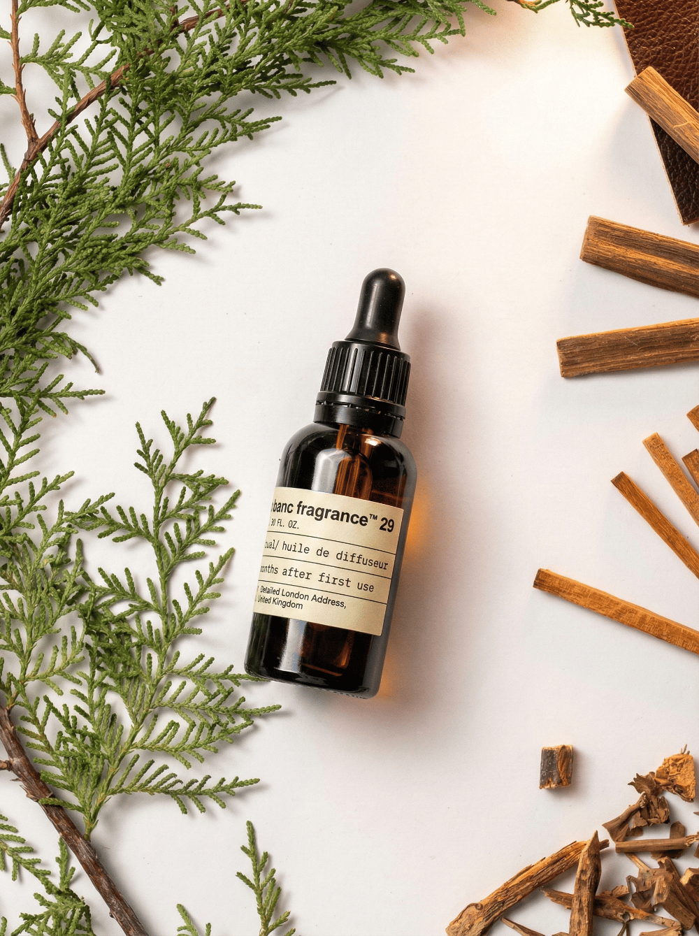 Charabanc Fragrance NO.29 Santal essential oil bottle styled with fresh green pine branches, sandalwood sticks, and leather accents for a cozy ambiance.