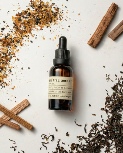 Charabanc Fragrance NO.17 Winds of Darjeeling essential oil bottle surrounded by loose black tea leaves, guaiac wood sticks, and amber resin grains.