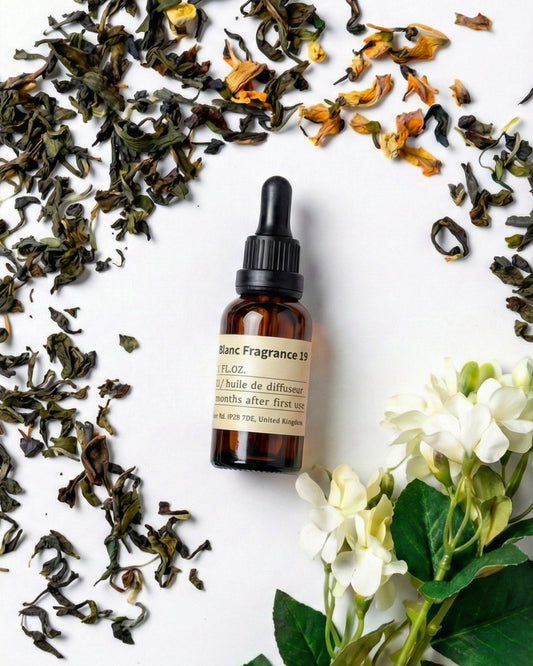 Charabanc Fragrance NO.19 All-Season Zen Tea essential oil bottle surrounded by loose green tea leaves and white jasmine flowers, evoking a serene tea ritual.