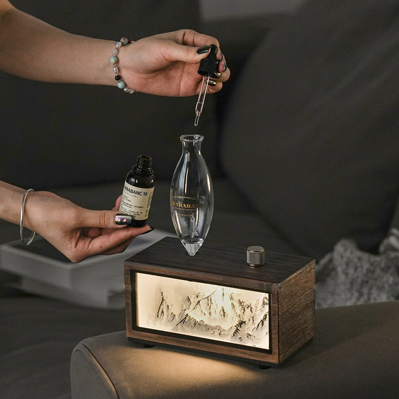 "A serene lifestyle shot of the Charabanc 'Alpine Edition' waterless nebulizer. The device features a sleek white console housing a detailed 3D mountain relief, illuminated by a warm golden light that mimics the alpenglow. Placed on a sofa next to a person reading, creating a perfect Zen meditation atmosphere."