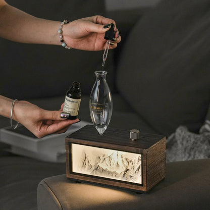 "A serene lifestyle shot of the Charabanc 'Alpine Edition' waterless nebulizer. The device features a sleek white console housing a detailed 3D mountain relief, illuminated by a warm golden light that mimics the alpenglow. Placed on a sofa next to a person reading, creating a perfect Zen meditation atmosphere."