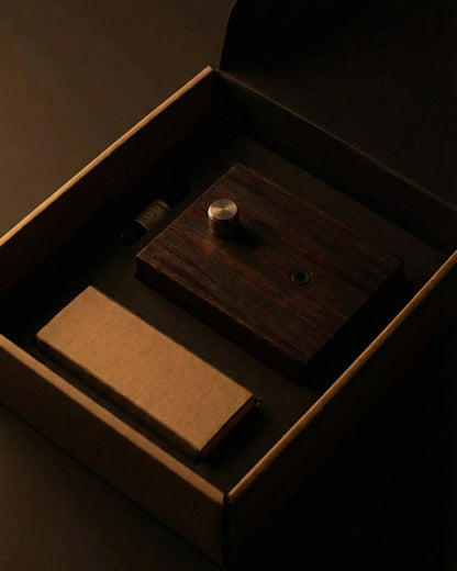 "A top-down overhead shot of the Charabanc Fragrance gift set in its open packaging. The dark wood diffuser base, a brown kraft paper box for the nebulizer, and a small essential oil bottle are neatly nestled in a precision-cut black foam insert, reflecting a minimal and sustainable luxury design."