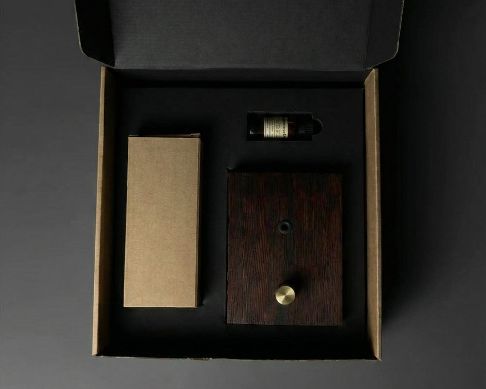 "A top-down overhead shot of the Charabanc Fragrance gift set in its open packaging. The dark wood diffuser base, a brown kraft paper box for the nebulizer, and a small essential oil bottle are neatly nestled in a precision-cut black foam insert, reflecting a minimal and sustainable luxury design."