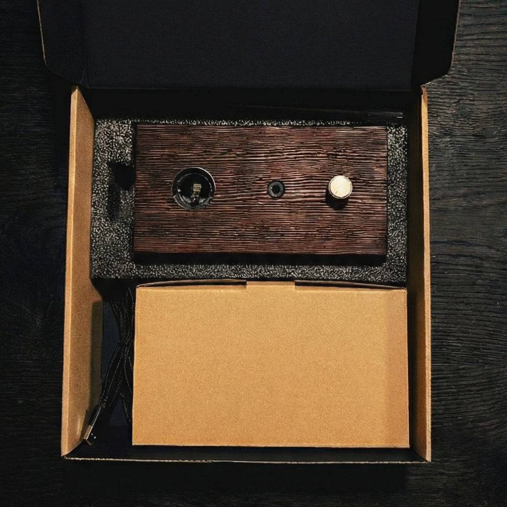 "A top-down overhead shot of the Charabanc Fragrance gift set in its open packaging. The dark wood diffuser base, a brown kraft paper box for the nebulizer, and a small essential oil bottle are neatly nestled in a precision-cut black foam insert, reflecting a minimal and sustainable luxury design."