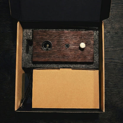 "A top-down overhead shot of the Charabanc Fragrance gift set in its open packaging. The dark wood diffuser base, a brown kraft paper box for the nebulizer, and a small essential oil bottle are neatly nestled in a precision-cut black foam insert, reflecting a minimal and sustainable luxury design."