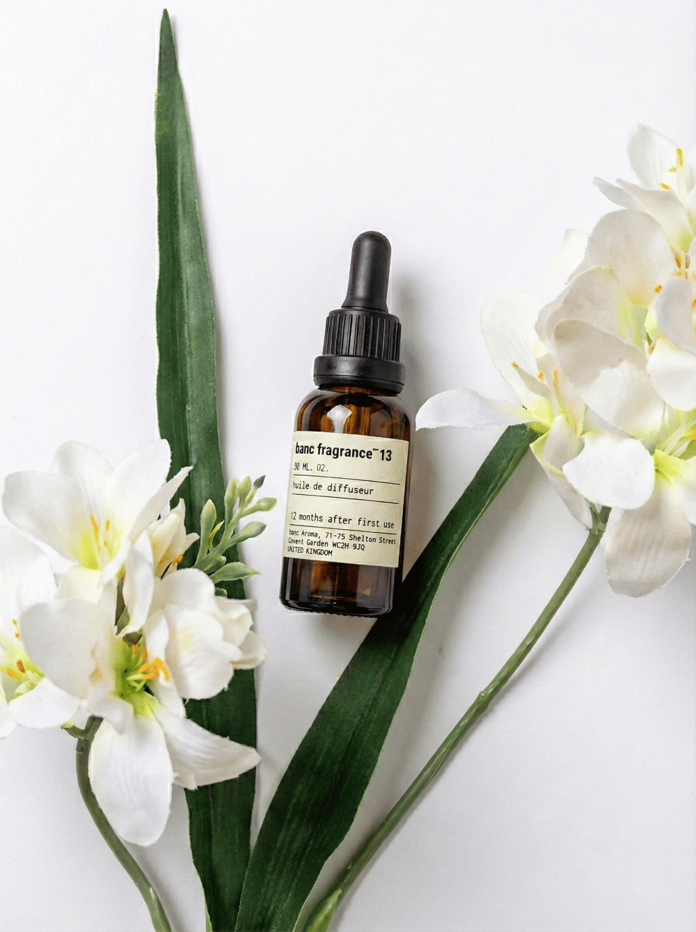 Charabanc Fragrance NO.13 Pear Freesia Whisper essential oil bottle displayed with elegant white freesia flowers and green leaves on a clean white background.