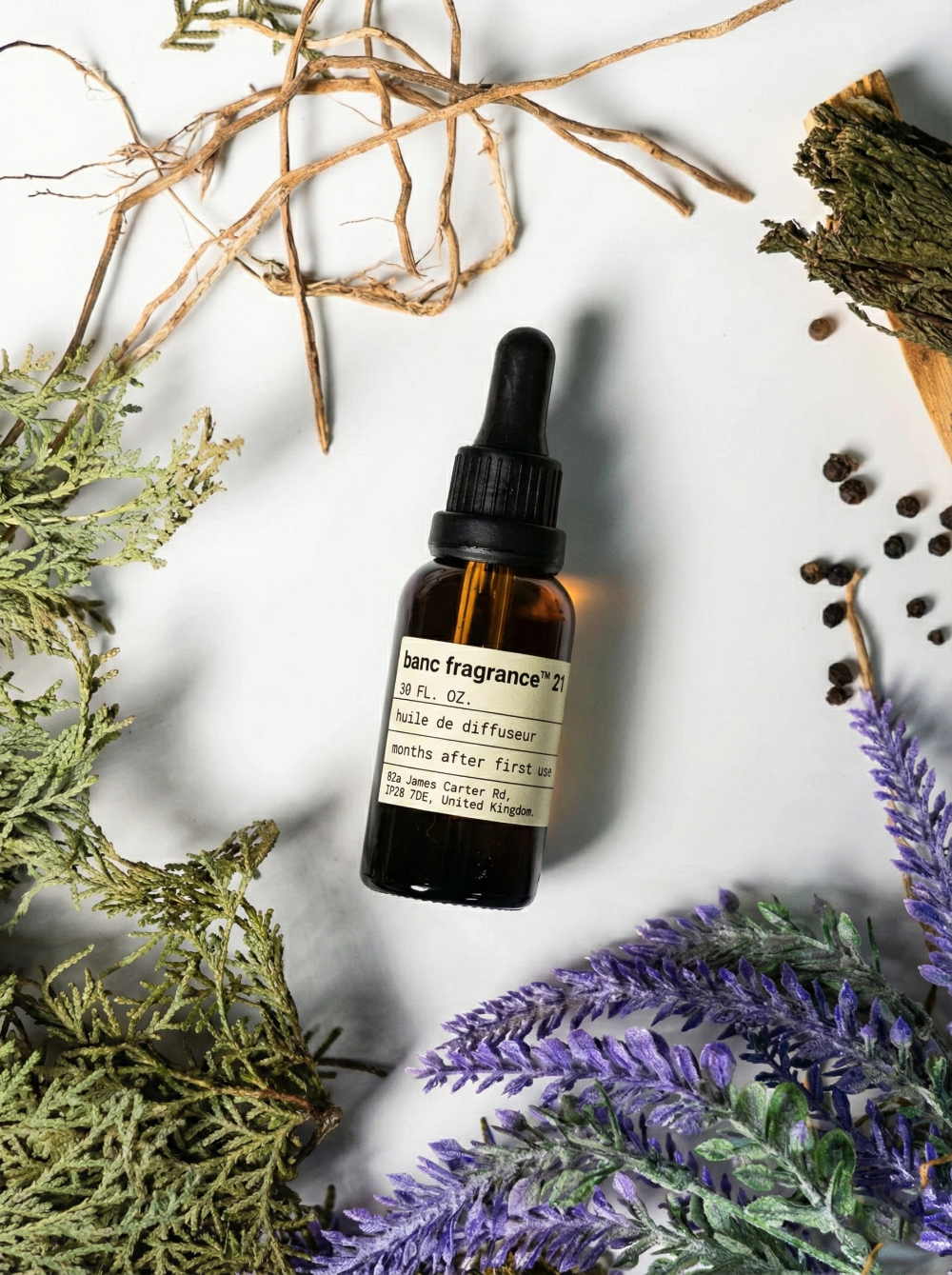 Charabanc Fragrance NO.21 Wild Horizon essential oil bottle surrounded by purple lavender sprigs, black peppercorns, green cedar branches, and rustic wood sticks on a clean background.