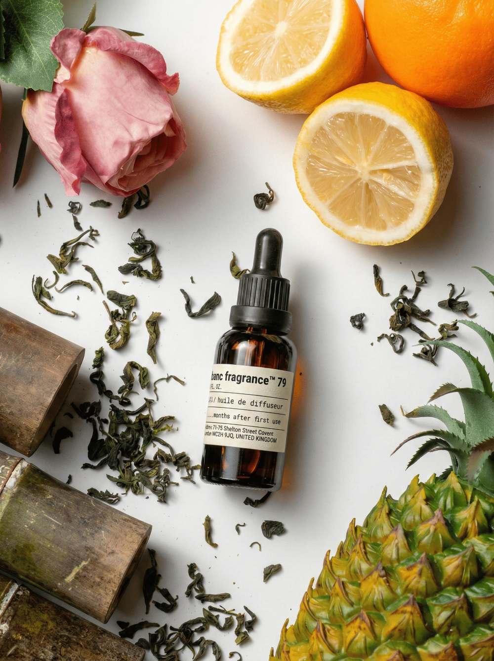 A bottle of NO.79 Shangri-La Essential Oil by Charabanc Fragrance featuring citrus and bamboo notes, displayed with fresh lemons, oranges, tea leaves, and bamboo stalks.